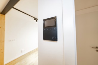 Wall intercom with display in a bright corridor next to a white door and warm parquet, house