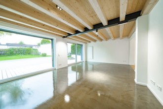 Open living room with wooden beam ceiling and polished concrete floor, flooded with light through