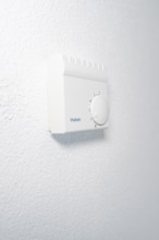 Wall thermostat with rotary knob on textured white wall in a quiet, bright atmosphere, house