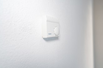 Close-up of a white room thermostat on a plastered wall in a bright, modern environment, house