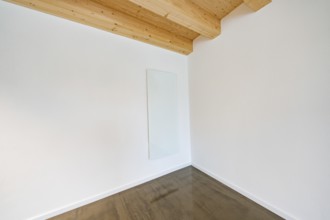 Bright corner with glass heating panel on white wall under wooden beam ceiling, reduced appearance,