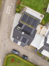 Top view of house with PV modules and carport green roof, two parked cars and curved road, house