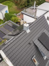 Angled aerial view of a house with PV systems on roof and carport, skylight and chimney in a quiet