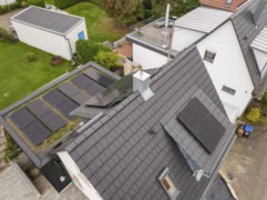 Aerial view of a modern house with PV on roof and carport with green roof, surrounded by gardens