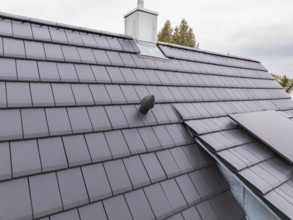 Detail of an anthracite-colored tile roof with roof vent and sheet metal connections under cloudy