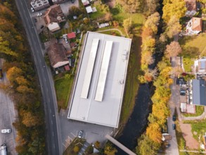 Aerial view of a sports hall in autumn-colored surroundings with adjacent river, Walter Lindner