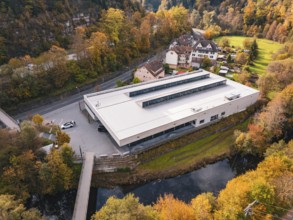 Sports hall nestled in an autumnal setting with a small river and bridge nearby, Walter Lindner