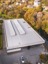 Flat roof of a sports hall surrounded by autumn-colored trees and nearby houses, Walter Lindner