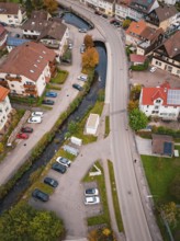 Aerial view of a small town with roads, parked cars and a river surrounded by autumn trees,