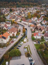 A bird's eye view of a village, showing narrow roads, lots of houses, autumn trees and cars,