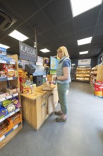 A woman stands at the cash register in a supermarket with snacks and products on the shelves, 24