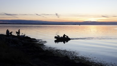 Angler on the beach during sunset, an angler docks on the shore with his inflatable boat and dog,