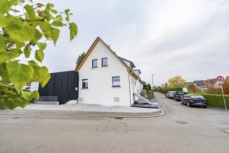 Side view of a bright residential building in a quiet settlement with parked cars and hedges, house