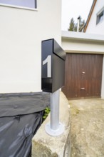 Close-up of a modern black mailbox in front of garage and plaster façade, house renovation, climate