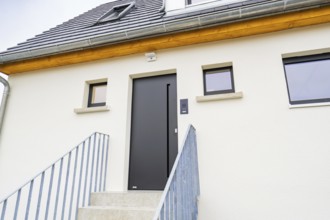 Modern house entrance with dark grey door and simple windows, staircase with metal railing, quiet