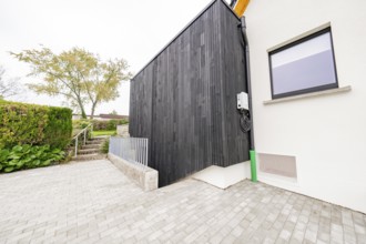 Modern house side with black wood paneling on paved driveway, house renovation, air conditioning