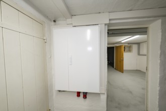 Simple basement corridor with white electrical distributor on plastered wall, objectively