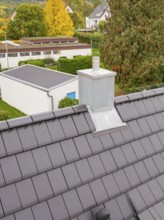Fireplace with metal cladding on anthracite-colored roof, view over the residential area, house
