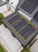 Detailed view of a green flat roof with raised black solar panels next to a bright wooden terrace,