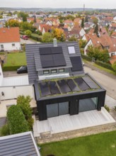 Aerial view of a modern single-family house with solar systems on a gable roof and green extension