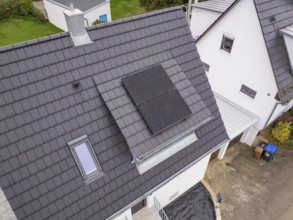Close-up of gable roof with two solar panels on a dormer with glass balustrade next to a skylight,