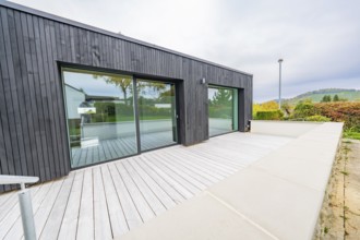 Large terrace with light wooden deck against black façade and sliding doors, wide views of autumn