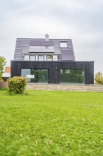 Single-family house with solar panels and black glass-fronted extension, large lawn in the