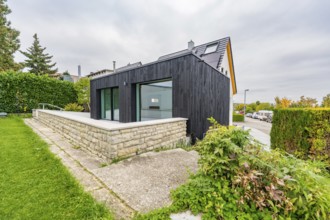 Black, modernly clad extension with large glass areas on lawn and stone wall in a quiet suburban