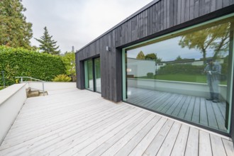 Minimalist extension with black wooden façade and large glass front opens onto a wide wooden