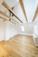 Light-flooded room under the roof with warm wooden floors and visible beam ceiling, house