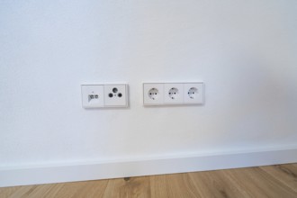 Modern sockets and connections neatly integrated into a white wall over oak floors, house