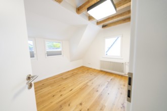Light-flooded attic room with oak floors and visible beams, freshly renovated and minimalistic