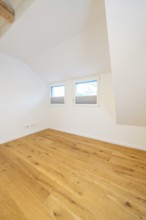 Cosy attic room with warm oak floor and two low windows, house renovation, air conditioning