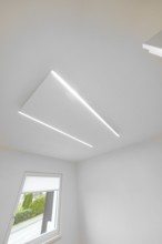 Modern white ceiling with two slim LED lines, geometric light detail near window, house renovation,