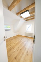Bright attic room with oak floor and visible beams, viewed through the open door, house renovation,