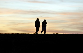 Walkers walk across a dike at sunset, Fehmarn Island, 13.10.2025, Fehmarn, Schleswig-Holstein,
