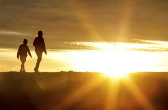 Woman and child walk across a dike on the island of Fehmarn at sunset, 13.10.2025, Fehmarn,