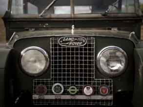 The front end of a 1950's Series One Land Rover, adorned with hunt club badges on the front grill,