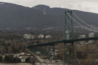 A long suspension bridge connecting a cityscape with mountainous surroundings under an overcast sky