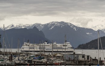 Ferry docked at a harbor with mountain range and snow in the background on a cloudy day in