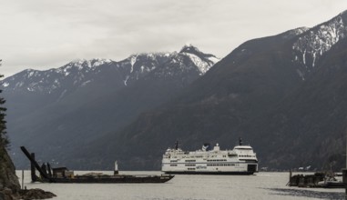 A ferry cruises through a scenic region with snowy mountains and cloudy skies in Horseshoe Bay,