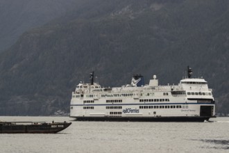 Ferry navigating across water with towering mountains under overcast skies in Horseshoe Bay, West