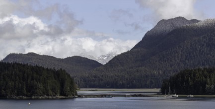 An expansive view of a lake bordered by forests and mountains under a cloudy sky in Tofino, British