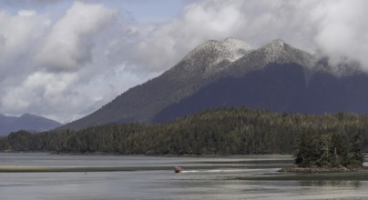 A small boat crosses a wide expanse of water with a backdrop of distant mountains and clouds in