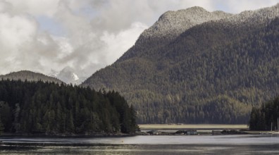 A panoramic view of mountains and forest surrounding a tranquil lake under an overcast sky in
