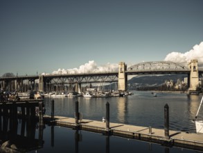 A wide bridge spans over a marina filled with boats, calm waters below in Vancouver, British