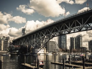 A grand bridge stretches over a busy harbor against a backdrop of clouds in Vancouver, British