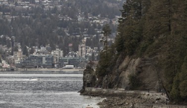 A rocky coastal path in Stanley Park with buildings and trees set against cloudy skies in