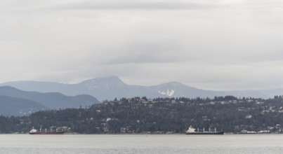 Distant view of ships passing by mountain-lined shores under cloudy skies in Vancouver, British