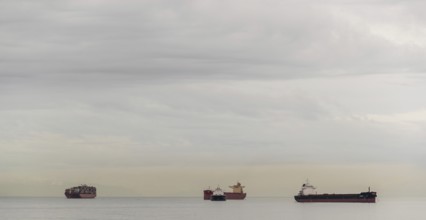 Several ships on the horizon beneath a blanket of clouds in Vancouver, British Columbia, Canada